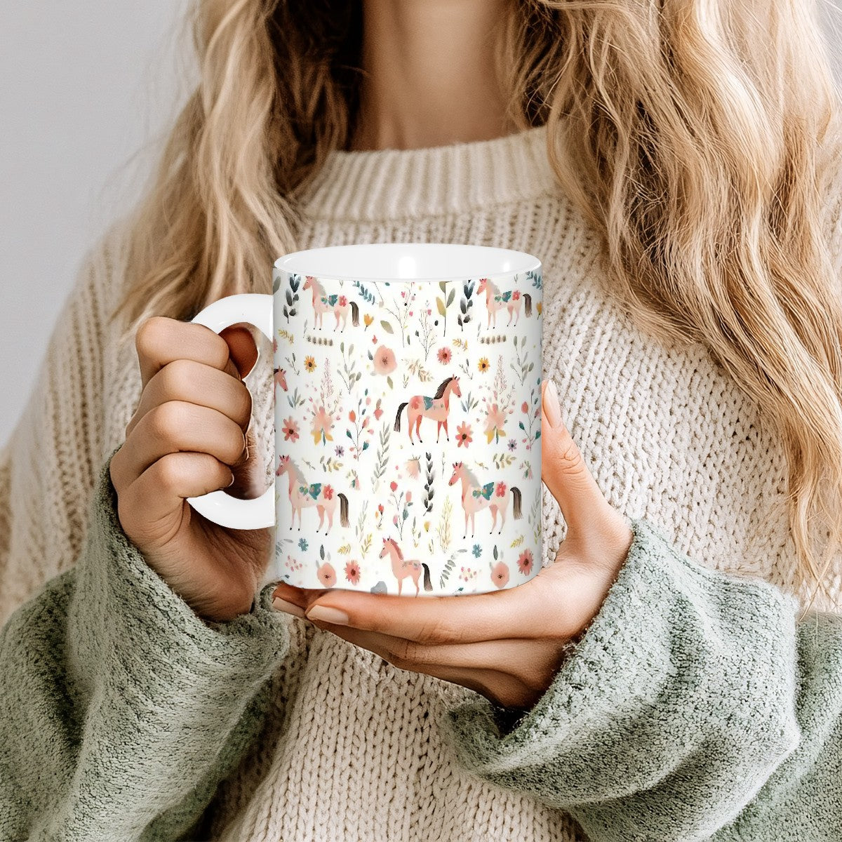 Person holding a mug with horse and floral pattern, wearing a beige sweater.