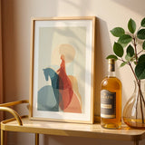 Framed abstract art on a table with a bottle of wine and a vase.