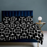 Bed with black and white patterned bedding against a gray wall.